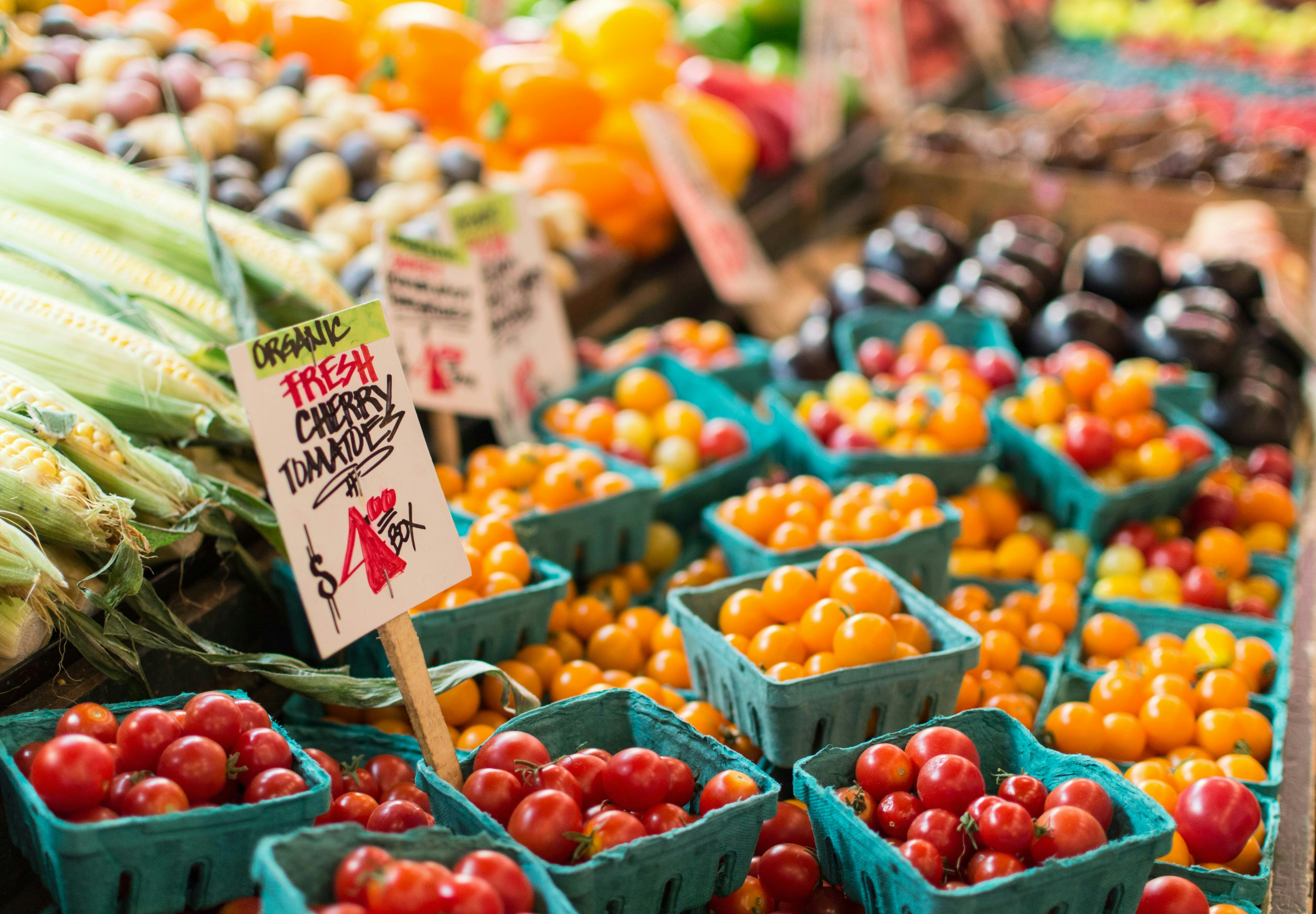 A farmer's market table full of vegetables and their price signs, with cherry tomato baskets and their price sign in the forefront.