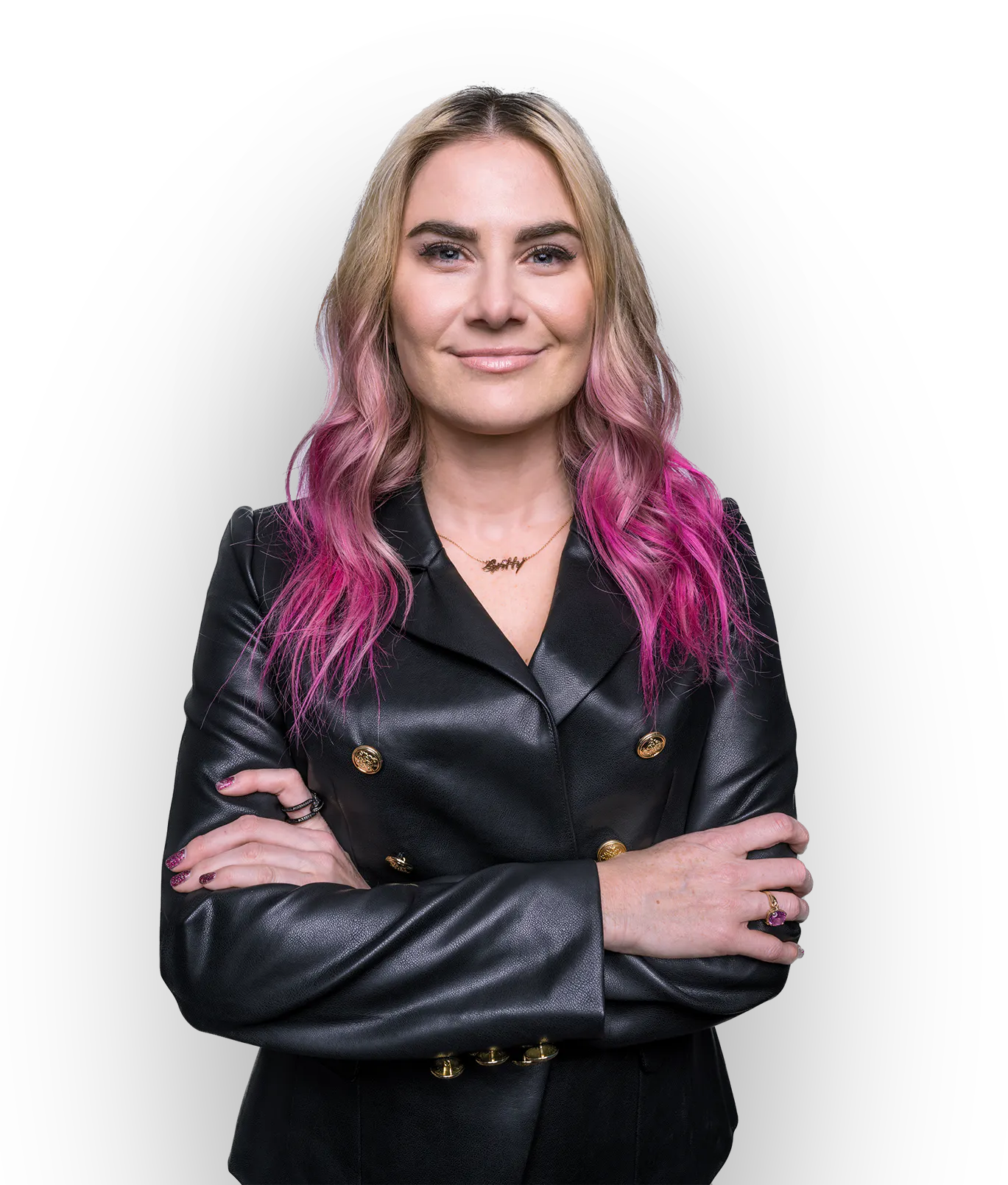 Shira Yevin has blonde hair with pink tips. She's wearing a black leather jacket and a gold necklace that says gritty. She has crossed her arms and is smiling confidently.