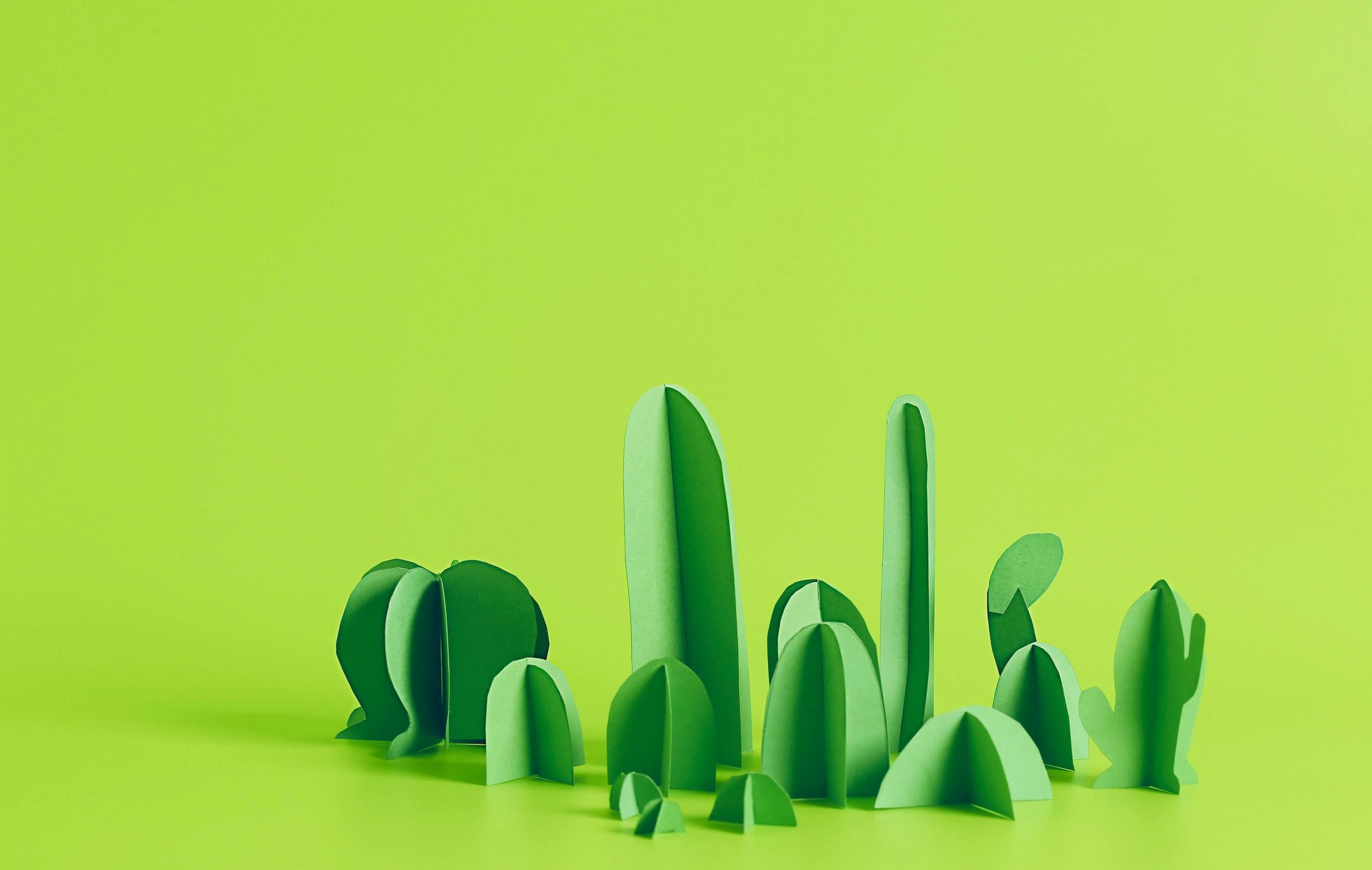 Bright green origami cacti on a light green surface.