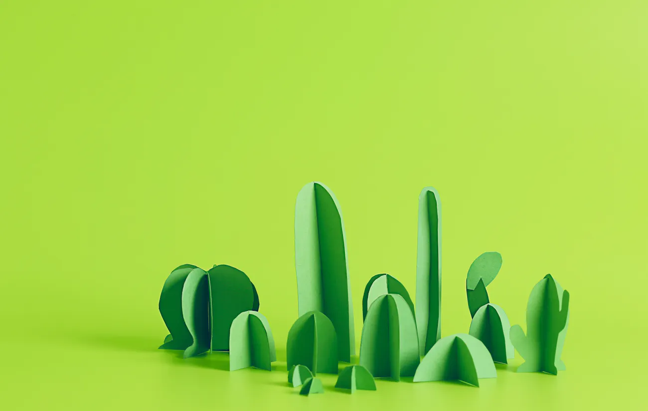 Bright green origami cacti on a light green surface.