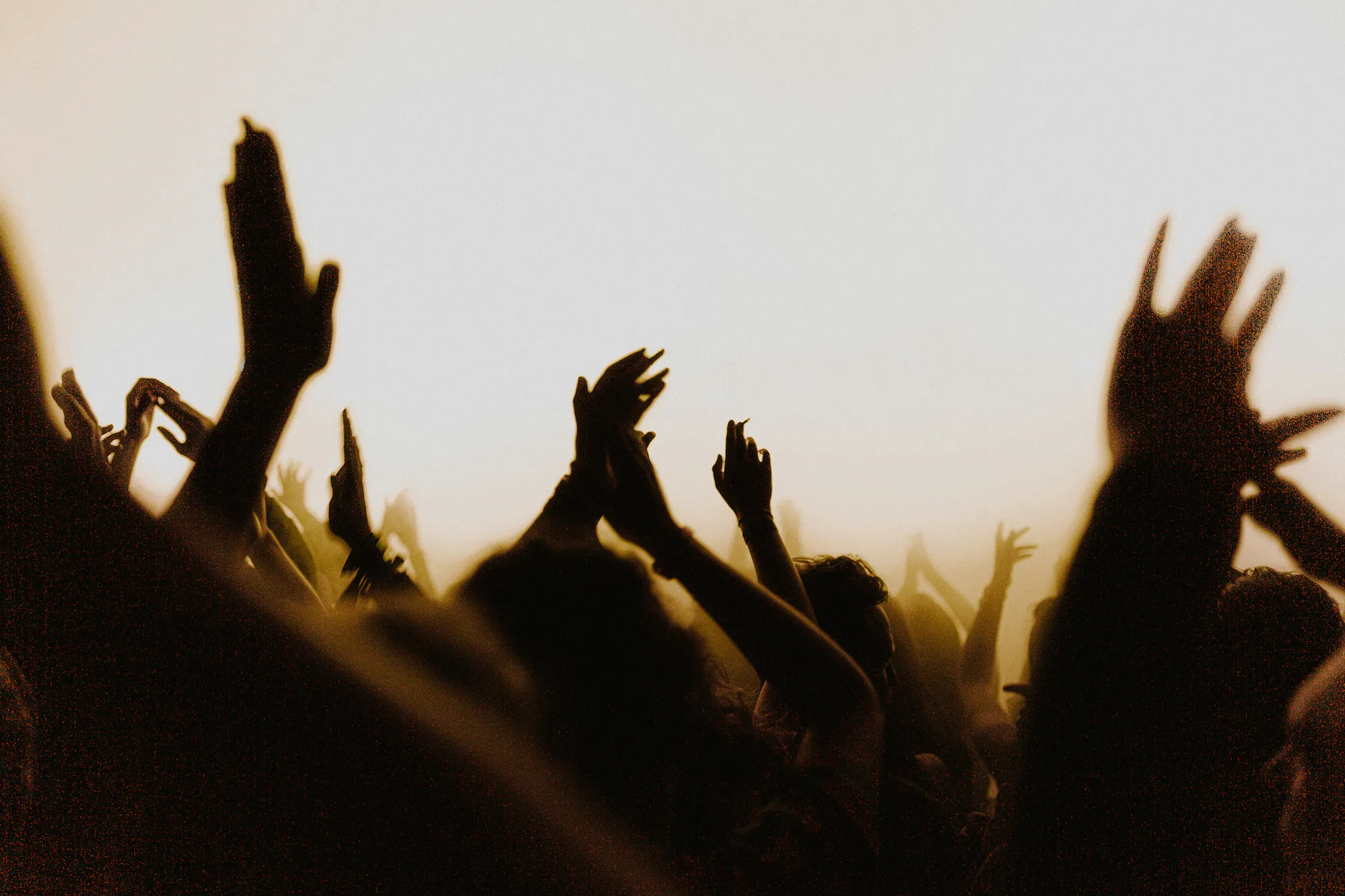 People clapping in a concert audience, silhouetted by a hazy light from the direction of the stage.