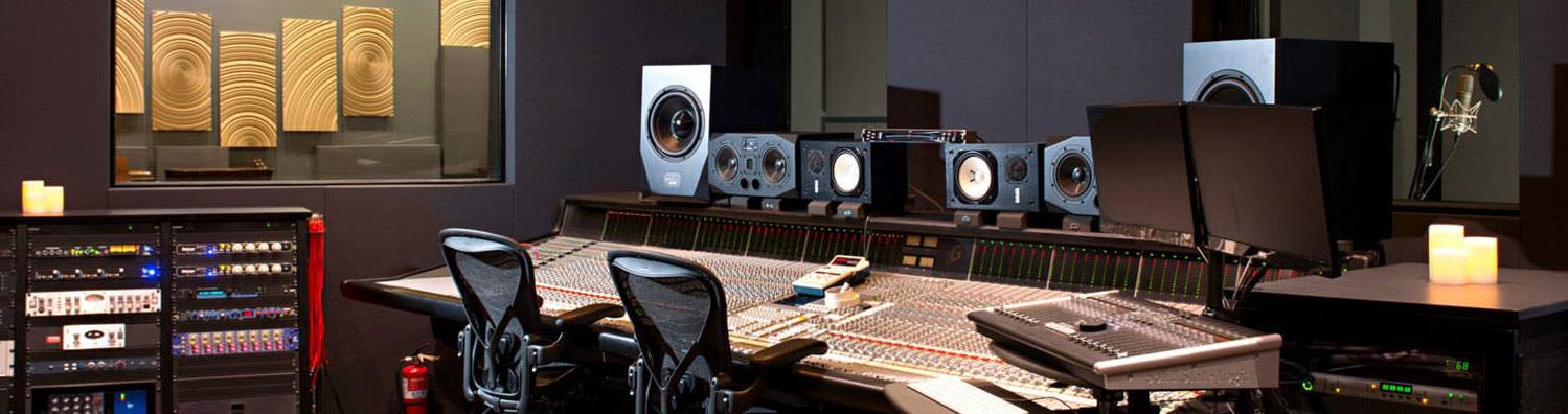 A music studio with two black chairs neatly in front of a mixing table and many speakers.