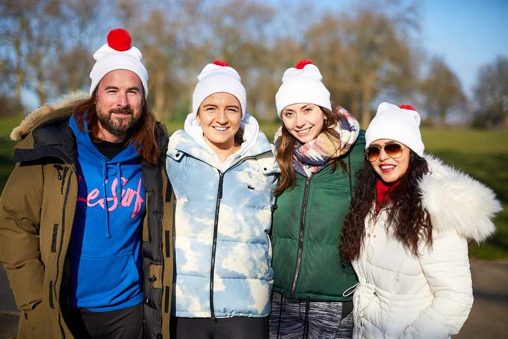 Four people smiling in the park in bobble hats