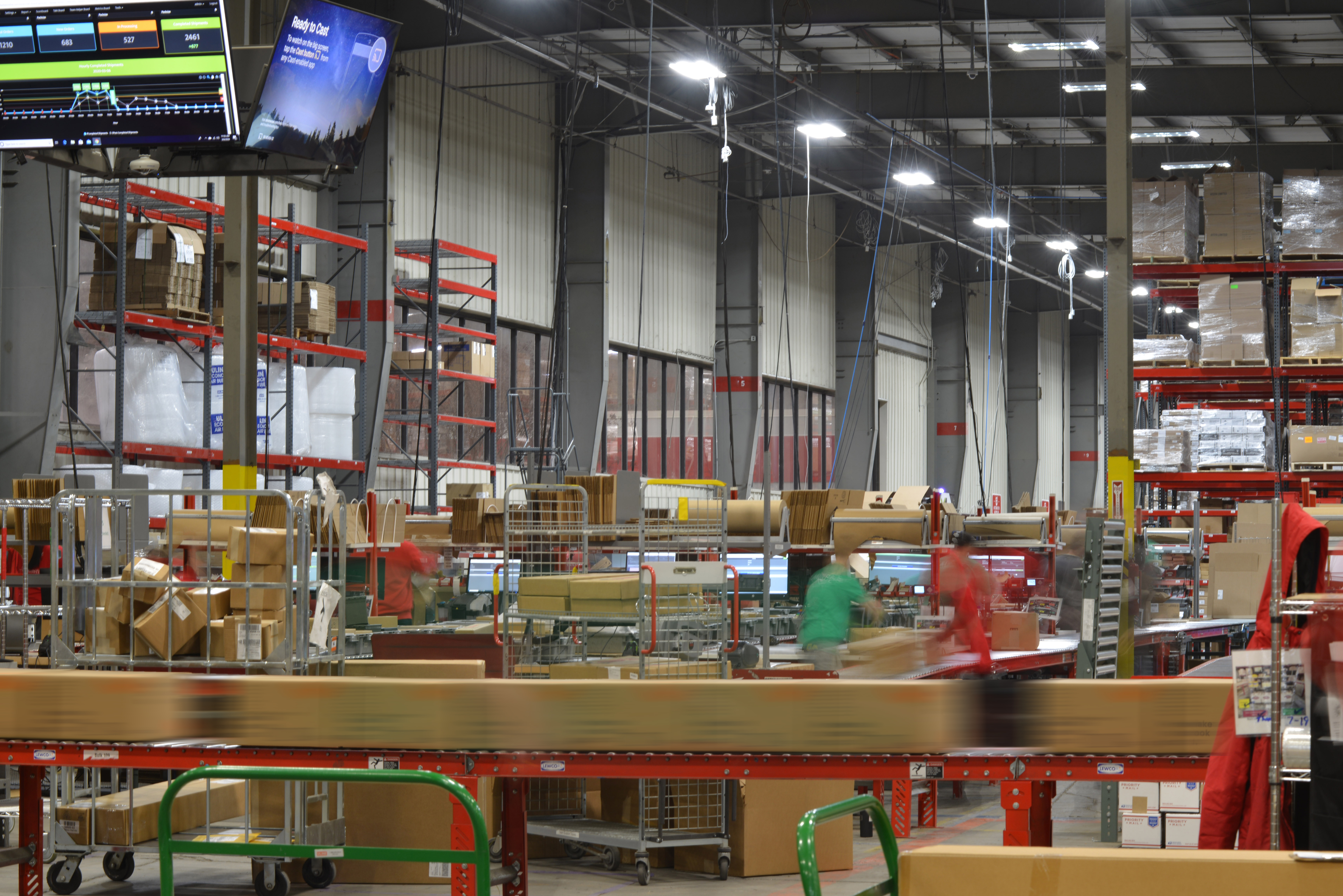 Several workers in red and green shirts moving quickly in a bright warehouse