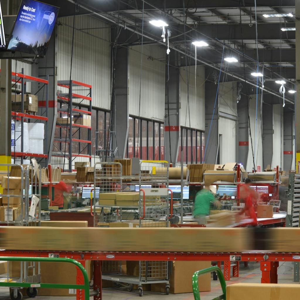 Several workers in red and green shirts moving quickly in a bright warehouse
