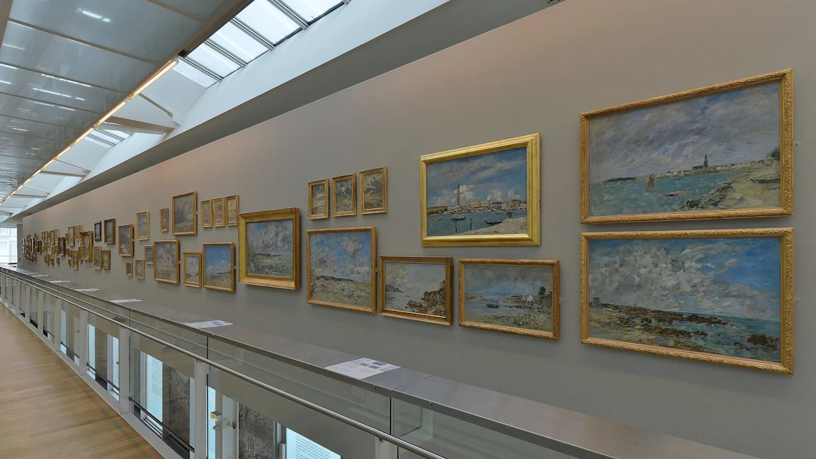 천장에서 빛이 들어오는 MuMa 전시실 벽에 Eugène Boudin 의 바다와 하늘 그림이 금빛 액자에 담겨 길게 줄지어 걸린 모습