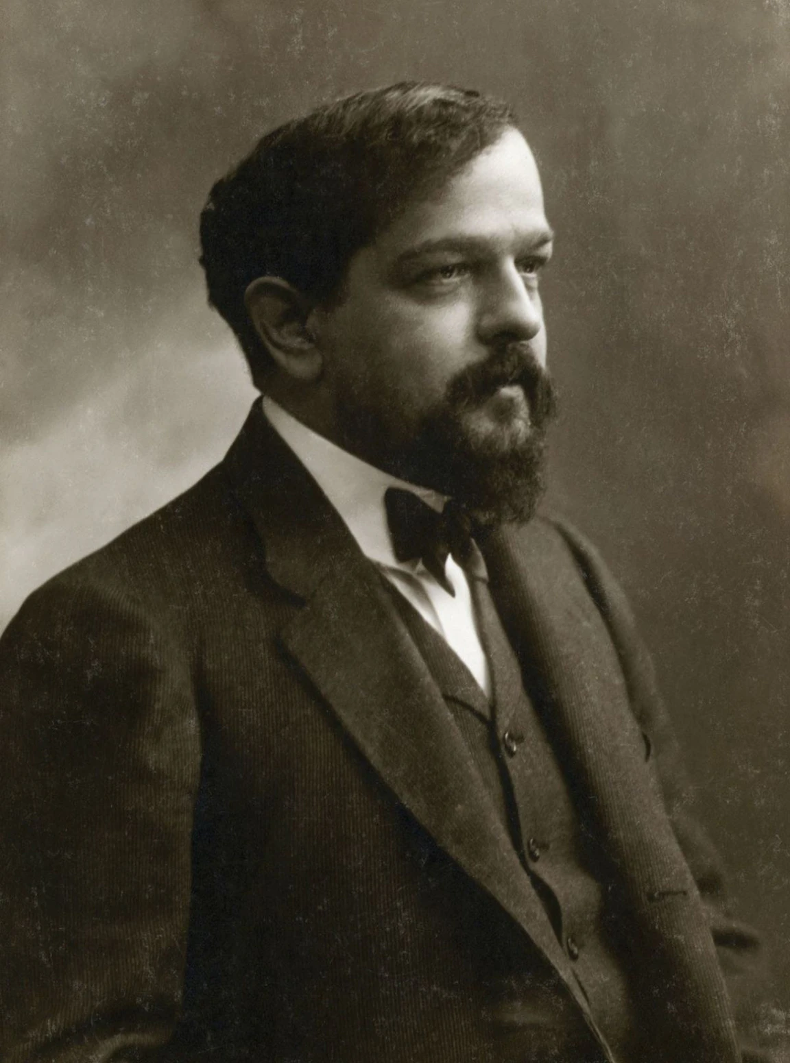 나비넥타이를 매고 정장을 입은 마흔여섯 살 Debussy 의 흑백 사진. 턱수염을 기르고 오른쪽을 바라본다