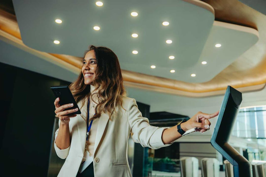 An image of a woman looking happy signing into a visitor management system in a lobby area