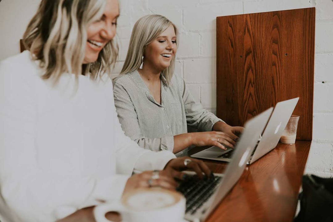 An image of two ladies remote working on their laptops in a coffee shop