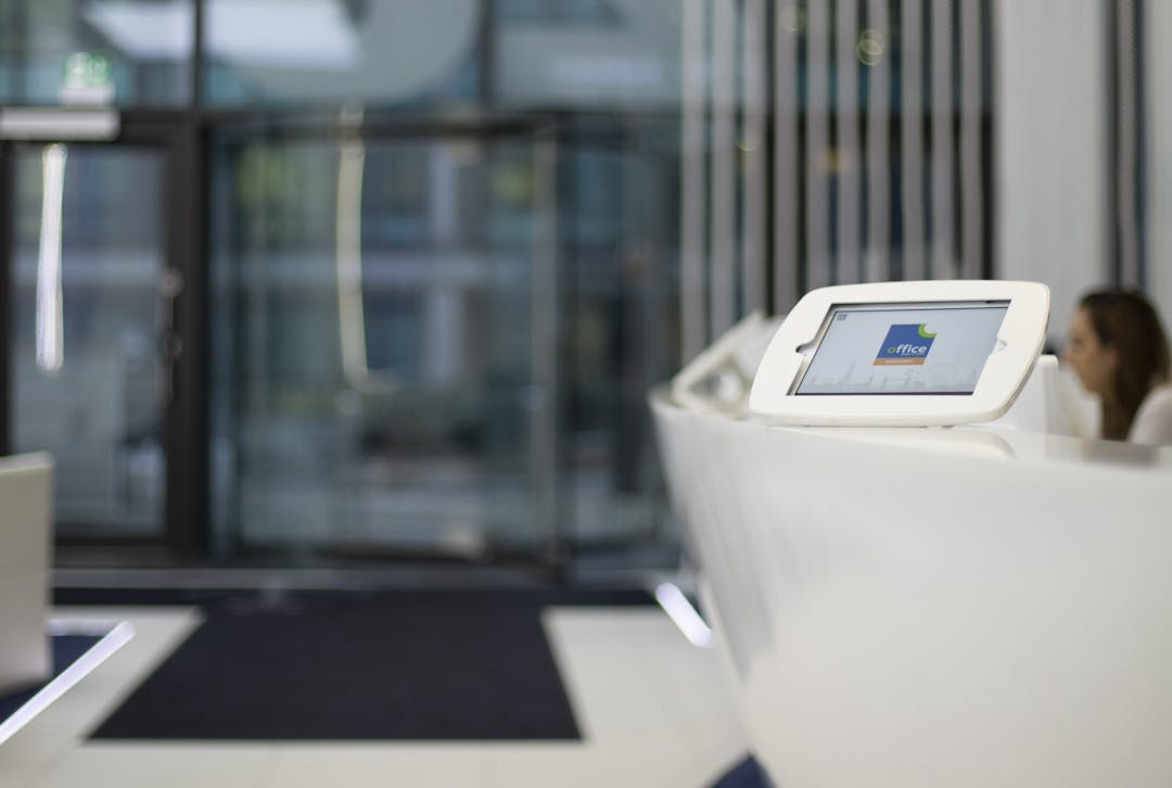 A photograph of a Sign In App iPad kiosk in a bright, modern office reception space.