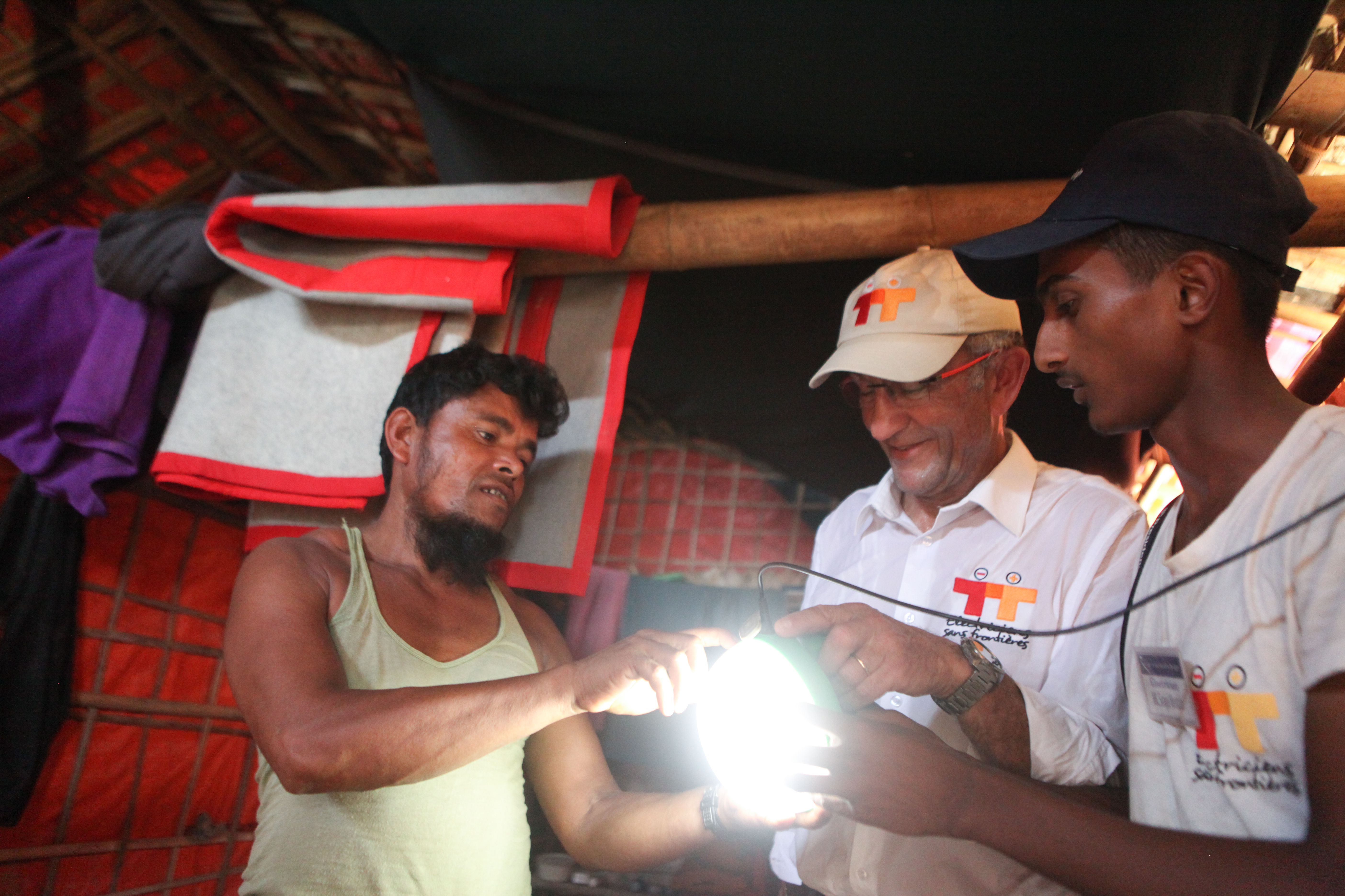 An Electriciens sans frontières volunteer and 2 other men hold a lamp