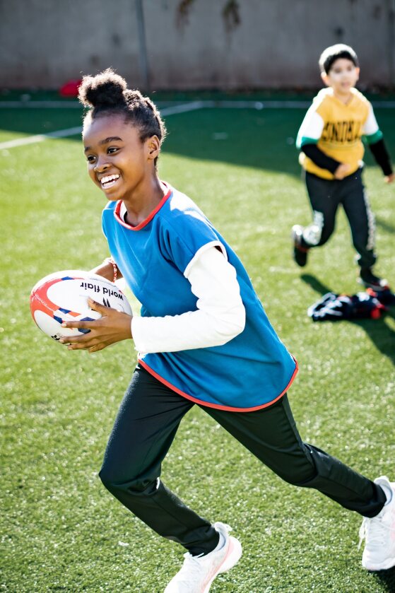 A child running and smiling while holding a rugby ball