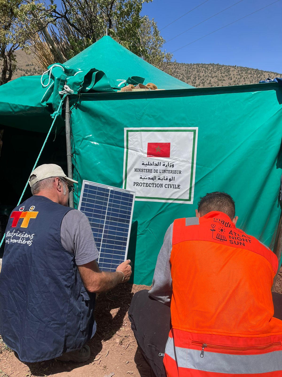 2 membres d'Électriciens sans frontières de dos, lors du tremblement de terre au Maroc, celui de gauche tient un panneau solaire