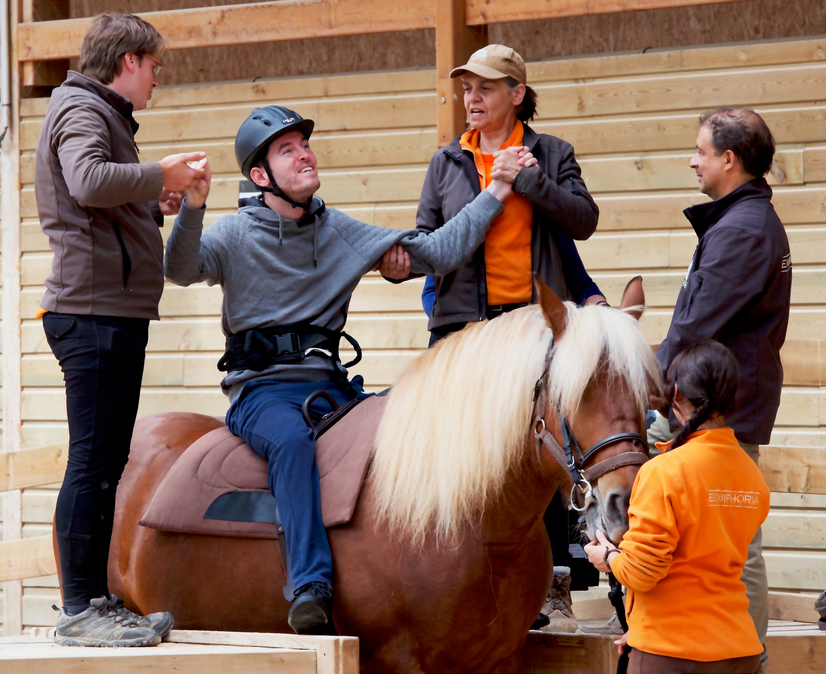 2 employés Équiphoria tiennent les mains d'un adulte en situation de handicap assis sur un cheval