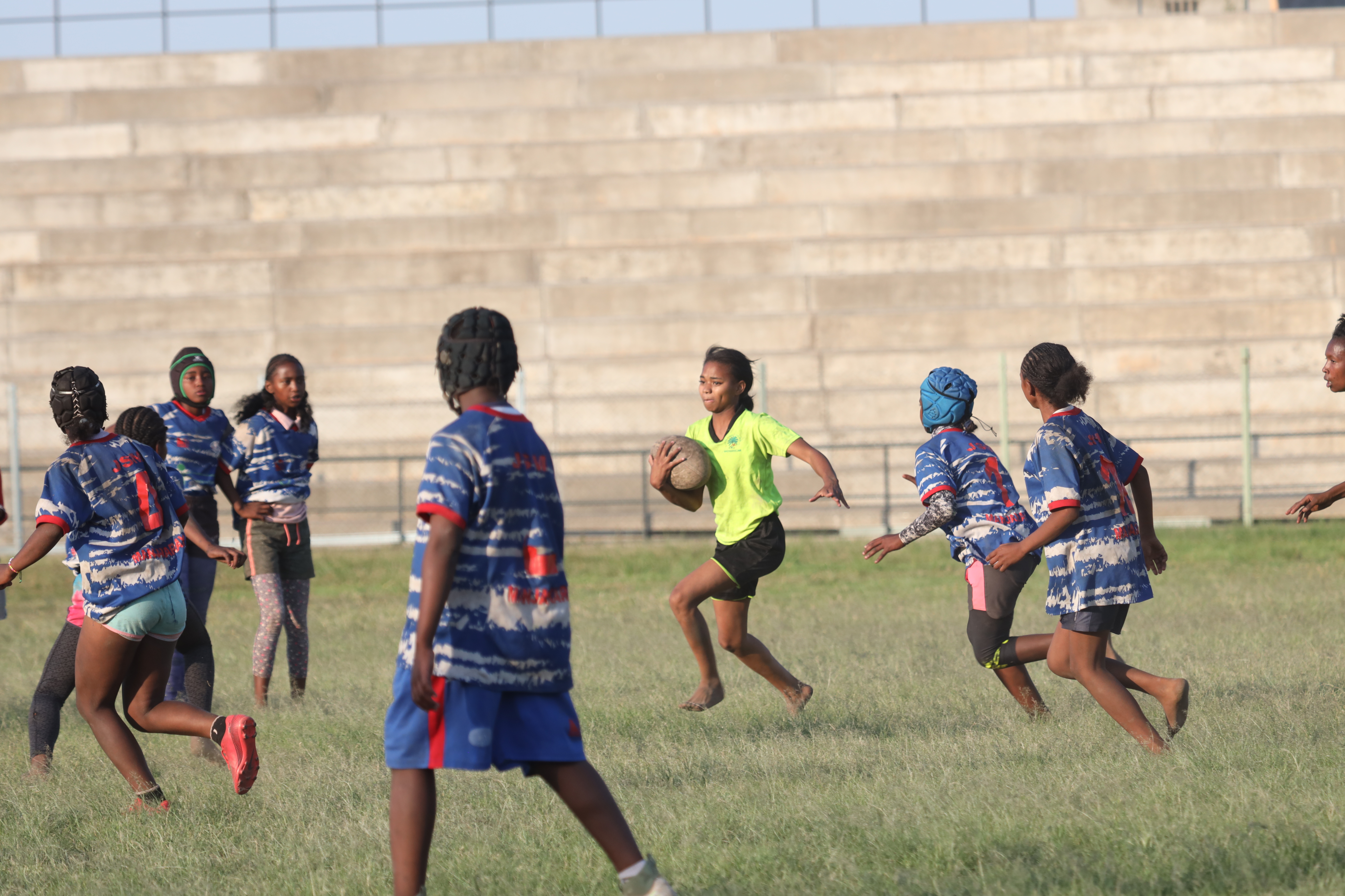 Des adolescents jouent au rugby sur un terrain et une fille court avec le ballon