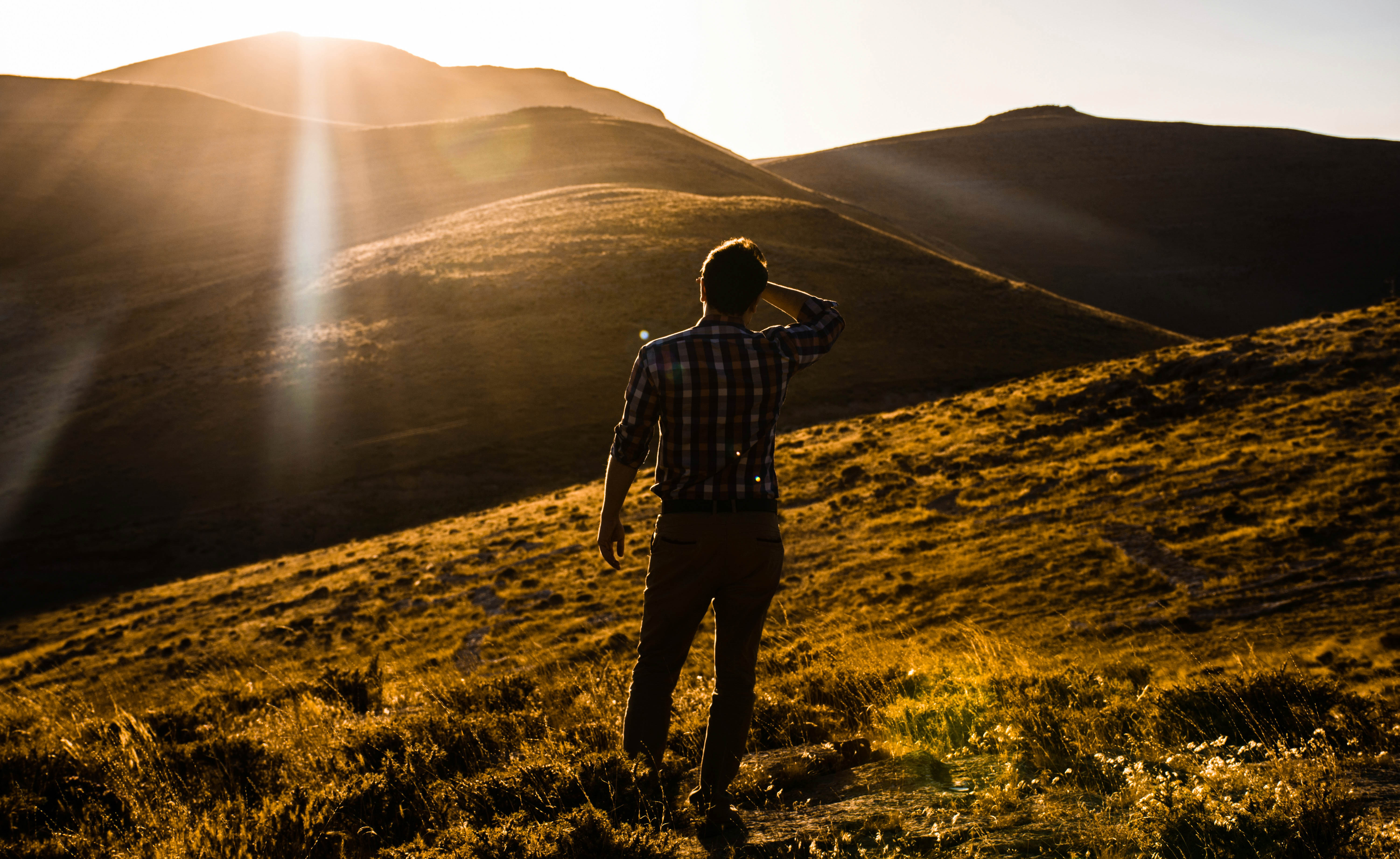 Homme dans la nature, sur des collines, et regardant l'horizon avec un coucher de soleil