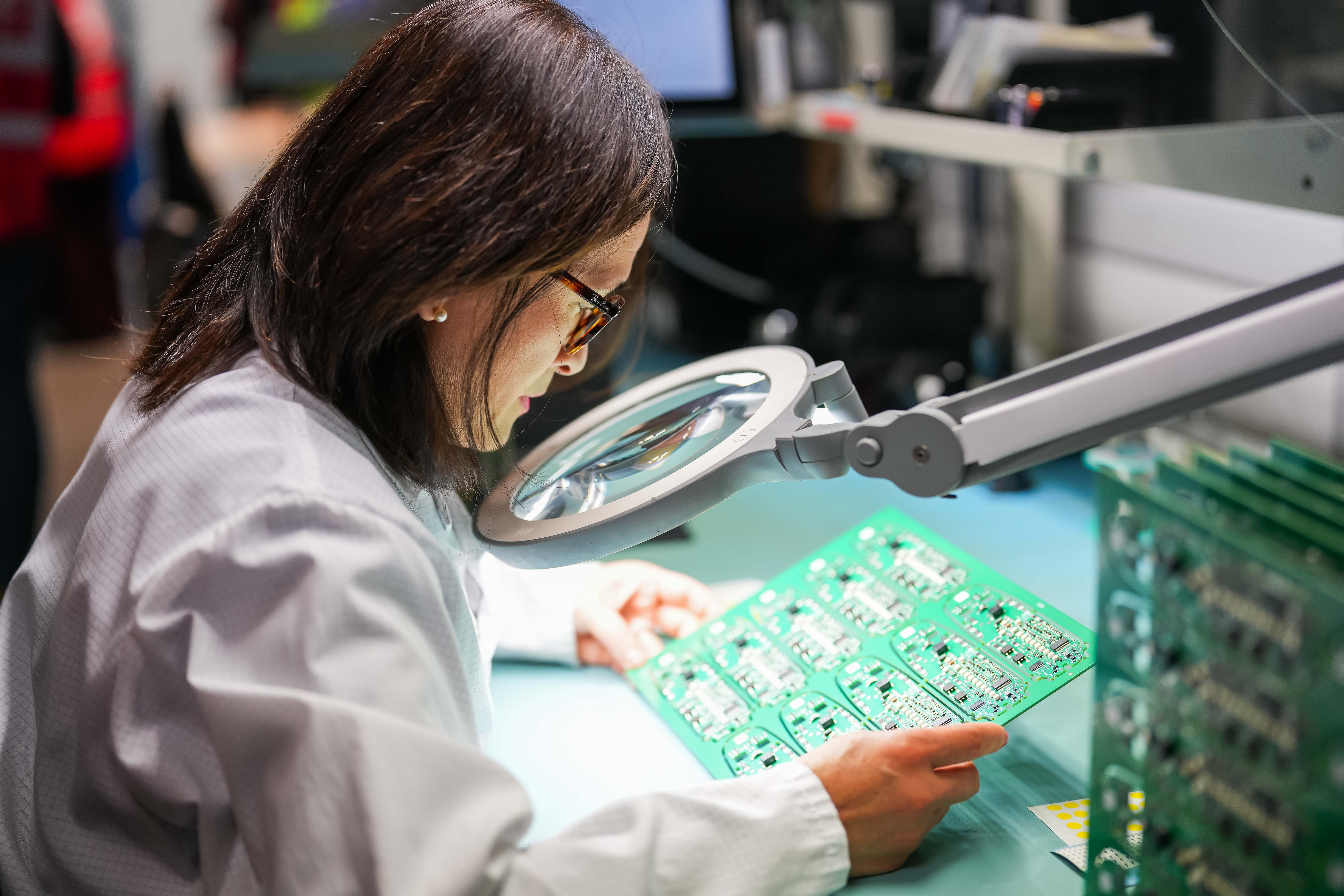Technician analyzing an electronic board with a large magnifying glass