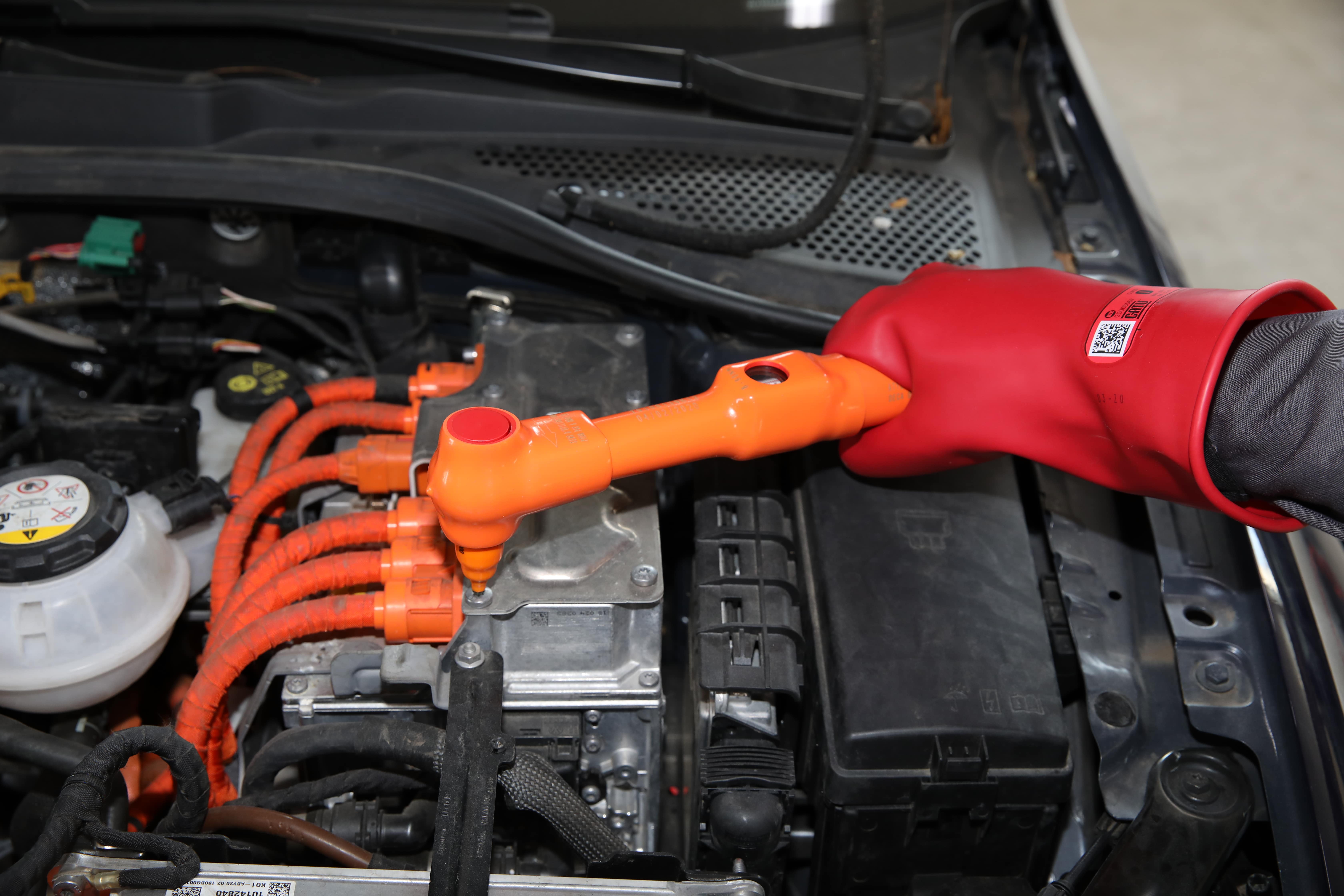 Main portant un gant de sécurité, et tenant un outil isolé, en train d'intervenir  sur le moteur d'une voiture électrique ou hybride