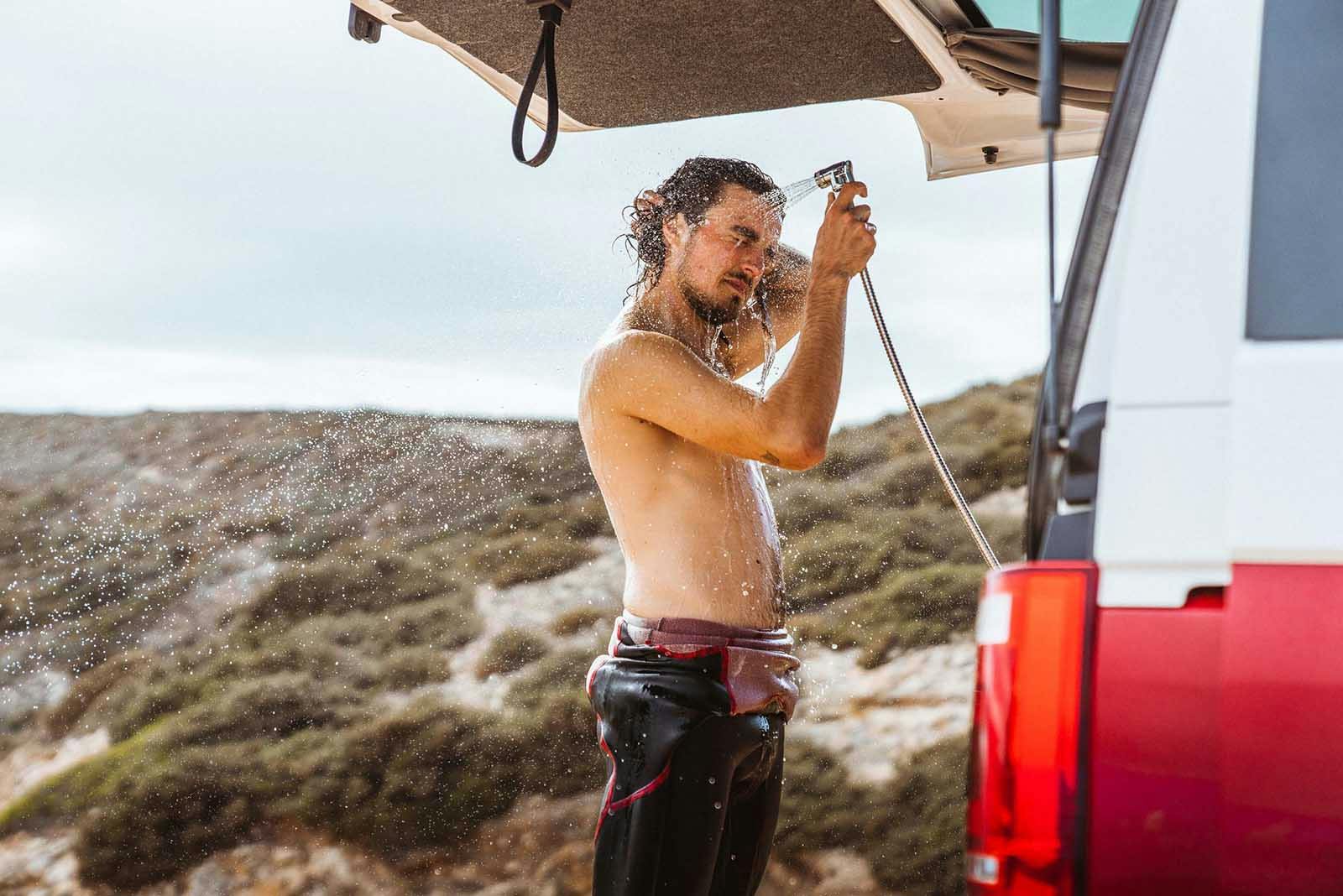 Surfer using an outdoor shower mounted on the rear of a Siesta Beach surf camper.