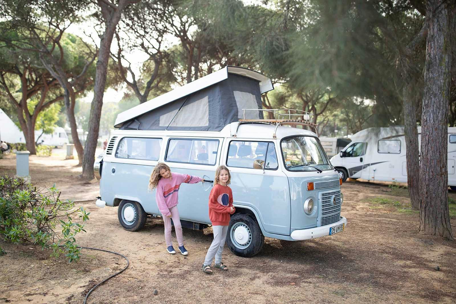 Children standing next to a vintage campervan at a campsite in Portugal.