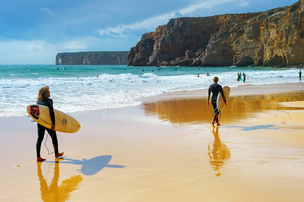 Zwei Surfer schlendern am Sandstrand entlang und genießen den Meerblick.