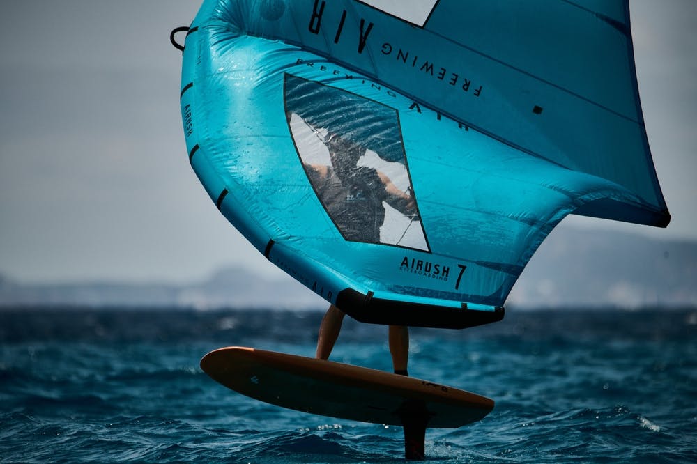 A person catches some air while wing foiling on the ocean under a clear blue sky.