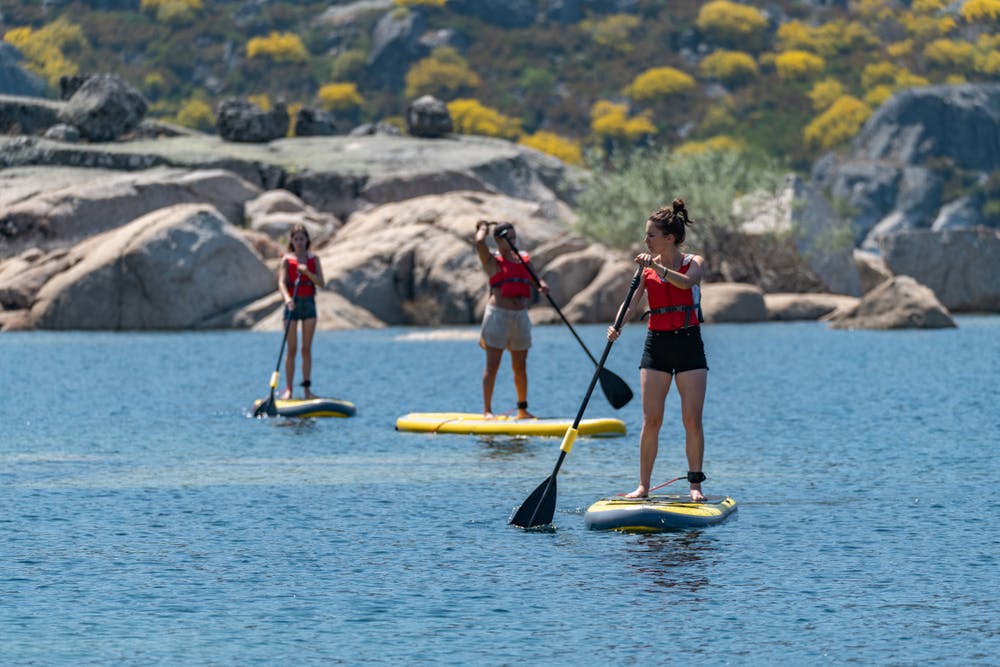 Três pessoas praticam stand-up paddle em águas calmas.