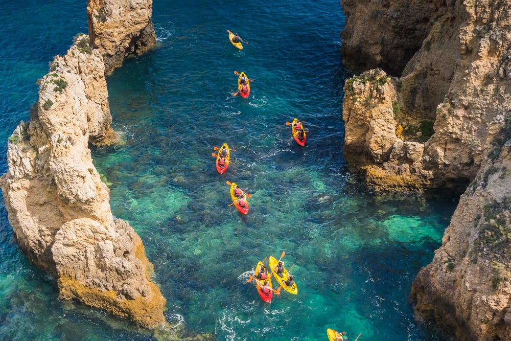 Caiaques exploram a costa algarvia em Portugal, com falésias pitorescas ao fundo.