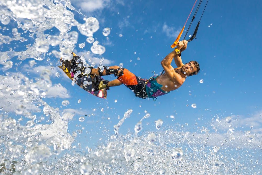 A kitesurfer rides the waves under a bright blue sky.