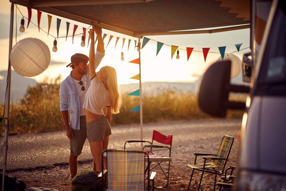 Under the awning of a campervan, a young couple enjoys a leisurely evening together free from the stress of daily life.