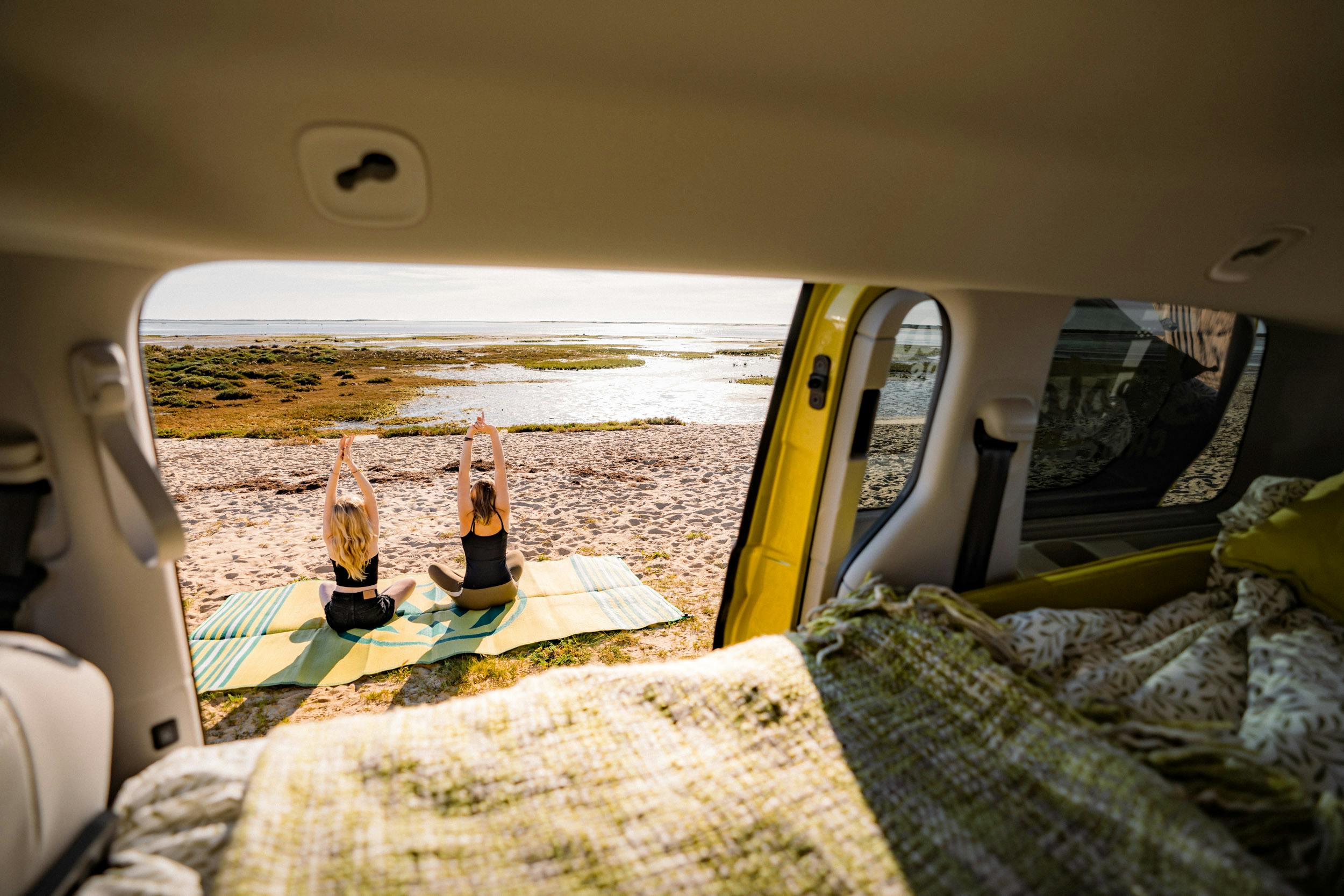 Zwei Freundinnen praktizieren bei einem Road-Trip durch ein unberührtes Naturschutzgebiet an der Atlantikküste Yoga.