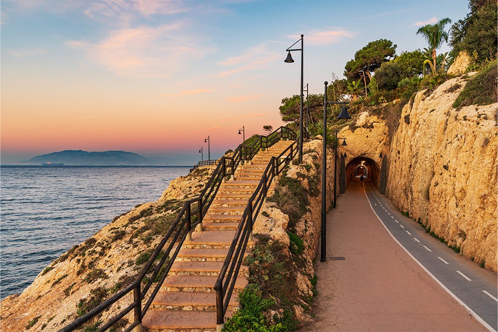 Uma ciclovia panorâmica e uma escadaria ao longo da Costa del Sol em Málaga, Espanha, ao pôr do sol.