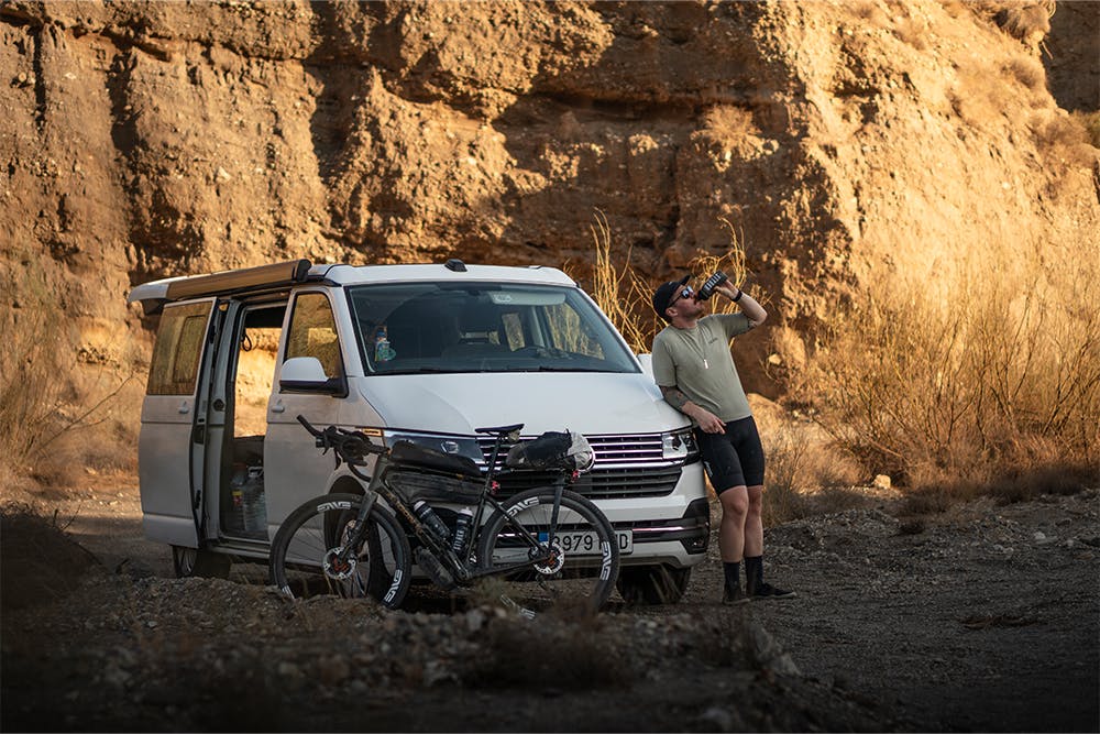 Un ciclista se toma un breve respiro del calor del desierto para descansar e hidratarse junto a su autocaravana antes de retomar el camino de grava.