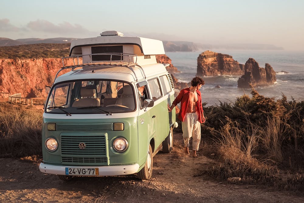 Un homme sort de son VW Kombi rétro Siesta Campers pour inspecter un endroit sablonneux.