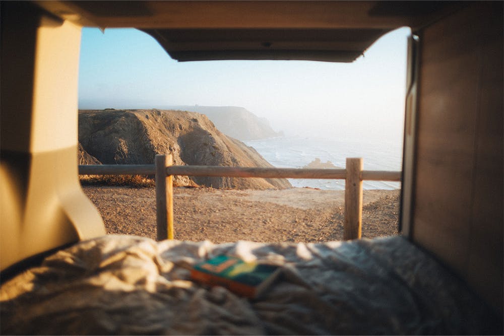 La porte arrière d'un camping-car s'ouvre sur la mer au lever du soleil.