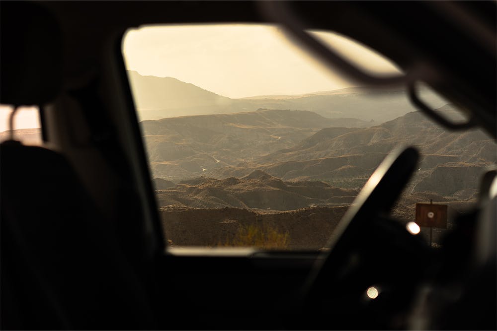 The driver's side window of a campervan looks out upon the layered Spanish Badlands.