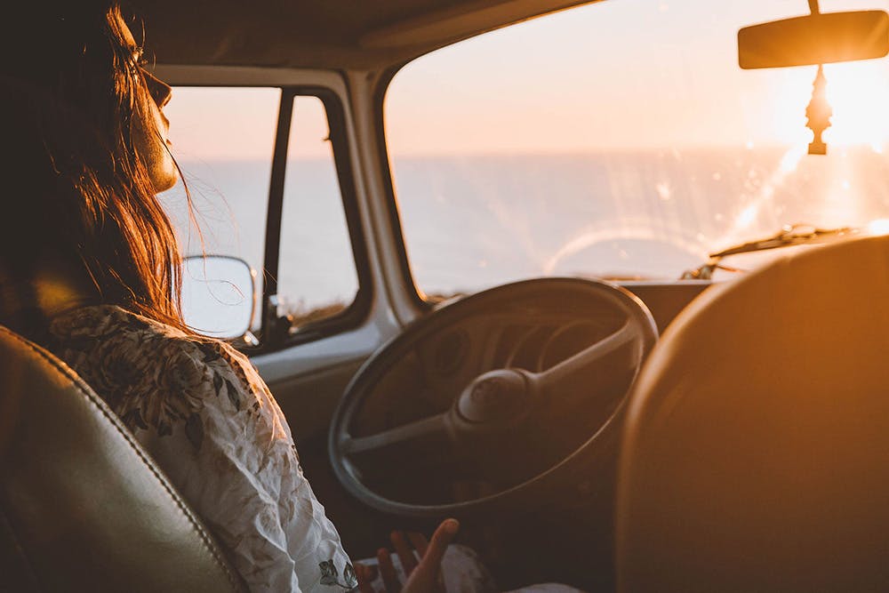 Uma mulher observa o pôr do sol de dentro de uma VW Kombi da Siesta Campers chamada Bahia.