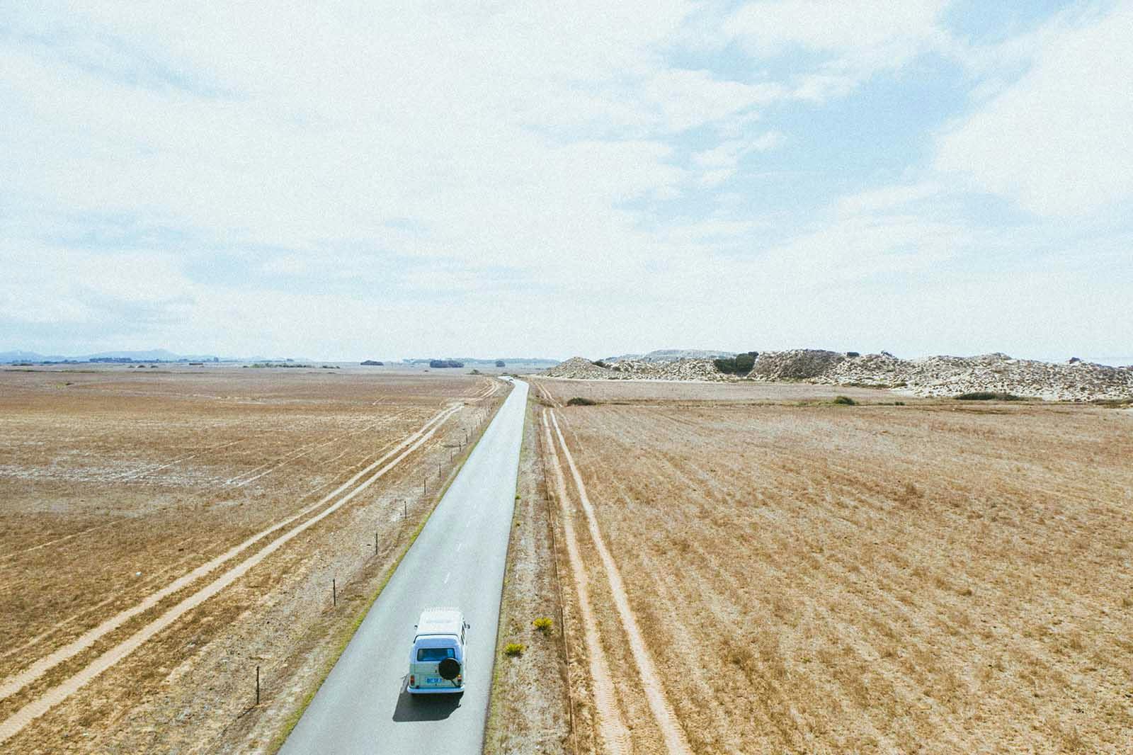 Uma pao de forma VW kombi vintage a percorrer uma estrada deserta em Portugal.