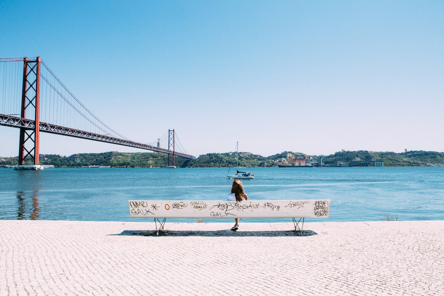 Mujer esperando a que el sol se ponga en el puente 25 de Abril con la estatue del Cristo Rei al fondo.