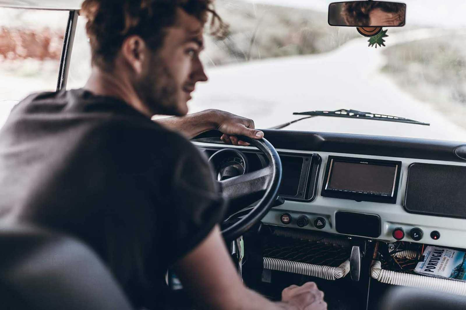 Begeisterter Fahrer eines klassischen Volkswagen T2 Campers streckt auf einer ruhigen portugiesischen StraBe seinen Kopf aus dem Fahrzeugfenster.
