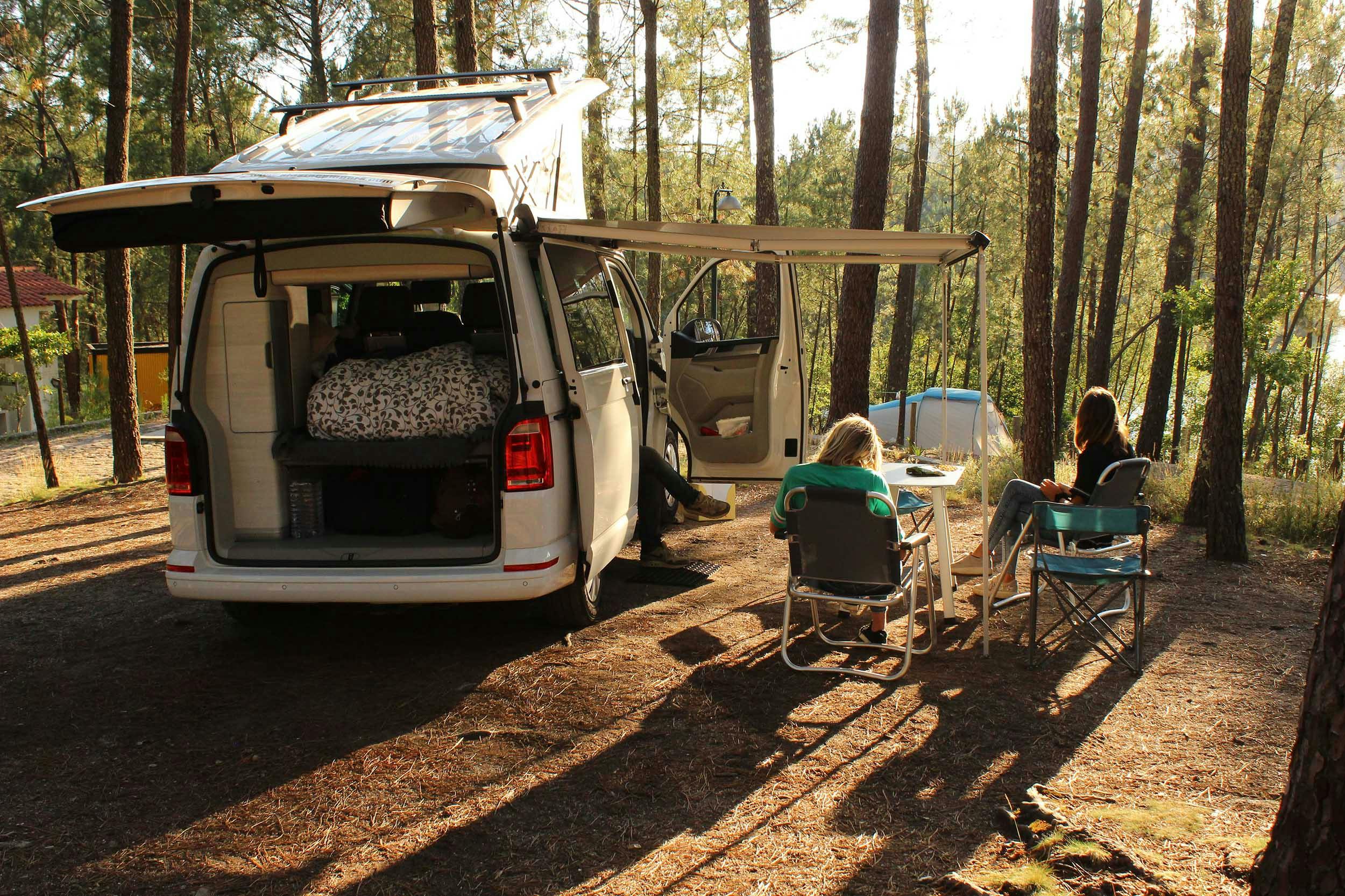 Unser VW California, geparkt auf einem Campingplatz in Portugal, umgeben von hohen Bäumen.