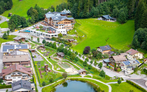 Luftaufnahme von Forstau mit Dorfhäusern, grünen Wiesen, einem kleinen Teich und umliegenden Wäldern in alpiner Landschaft.