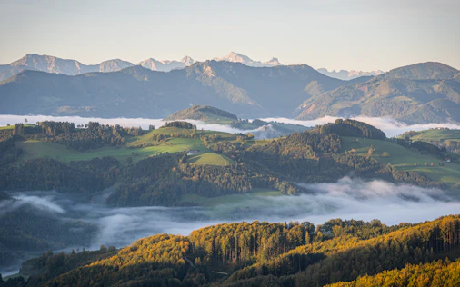 Nebel über sanften Hügeln und Tälern im Salzburger Land mit Bergketten im Hintergrund.