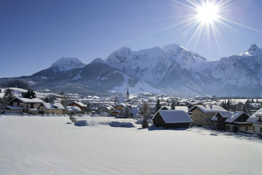 Winter mountain landscape with a snow-covered village in the valley, surrounded by high mountains under bright sunshine.