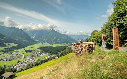 Das Bild zeigt eine ruhige Hanglage mit weitem Blick über grüne Täler und sanfte Berglandschaften. Eine Terrasse mit Sitzbereich lädt zum Entspannen ein und vermittelt ein Gefühl von Freiheit, Natur und exklusiver Wohnqualität.