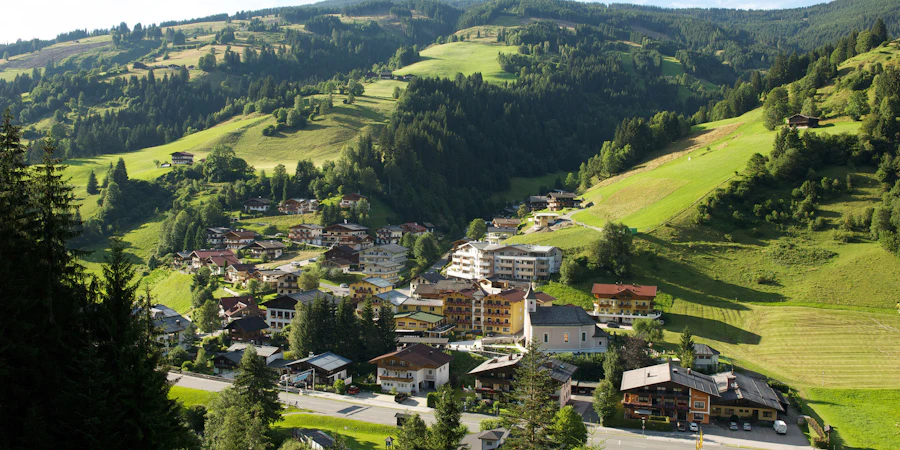 The image shows an idyllic alpine village nestled in gentle green hills. The scattered houses and open landscape convey a sense of tranquility connection to nature and an authentic rural lifestyle.