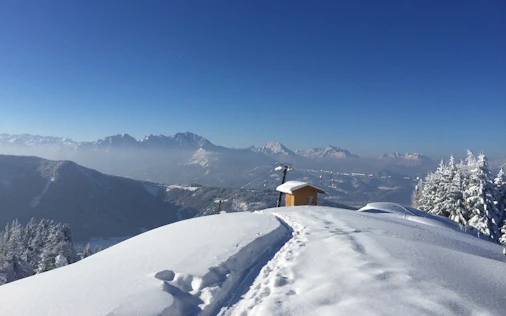 Verschneite Berglandschaft mit weitem Ausblick auf die Alpen, klarer Himmel und ruhige, unberührte Natur – ein Ort der Erholung und beeindruckenden Weite.