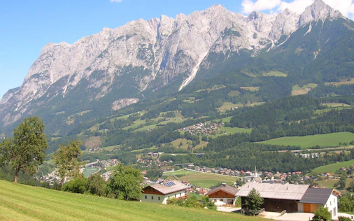 Idyllische Alpenlandschaft mit saftig grünen Wiesen, vereinzelten Häusern und beeindruckender Bergkulisse – ruhig, naturnah und mit hoher Lebensqualität.