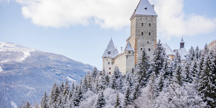Majestätische Burganlage auf einem verschneiten Hügel mit Blick auf die umliegende Berglandschaft – eindrucksvoll, ruhig und von zeitloser Schönheit.