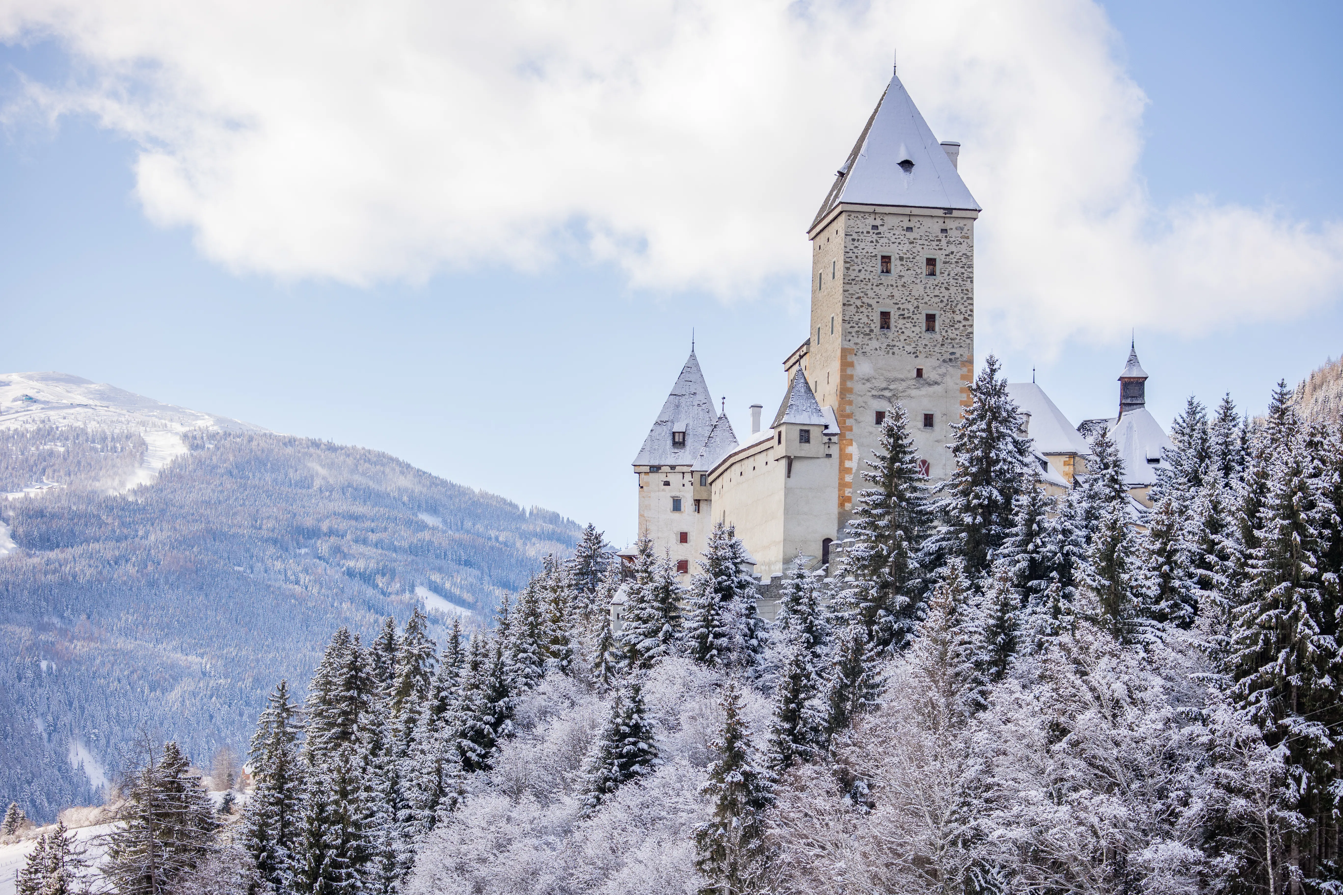 Majestic castle complex on a snow-covered hill overlooking the surrounding mountain landscape – impressive, serene, and of timeless beauty.